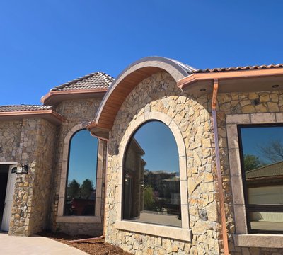 Finished copper seamless gutters wrapping the arched entryway of a Northern Colorado stone home