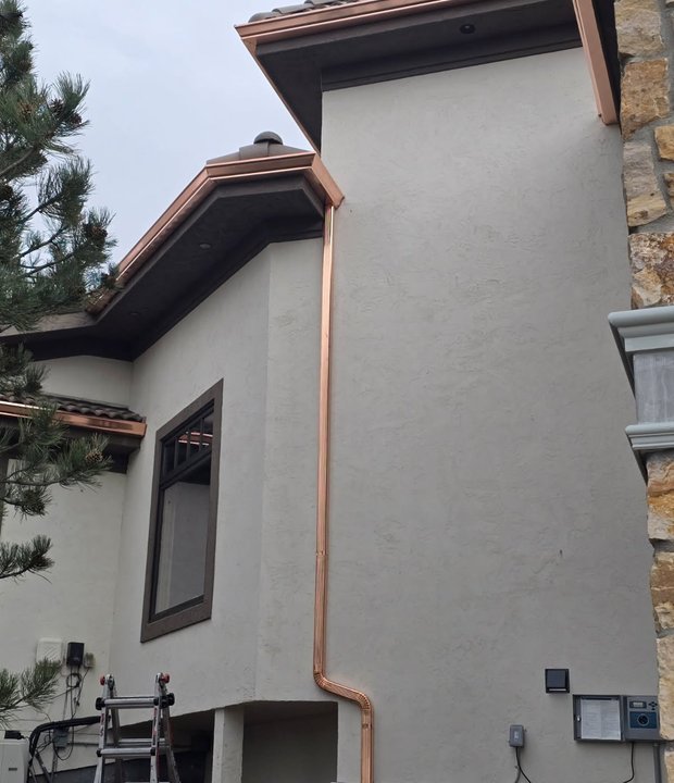 Copper downspout feeding a decorative rainwater feature on a stucco home