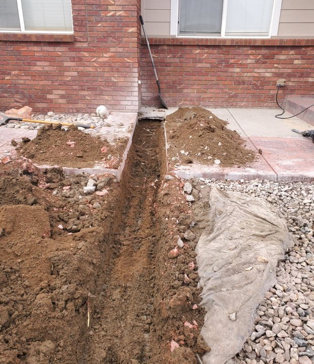 Buried drainage trench carrying downspout water away from a brick home foundation